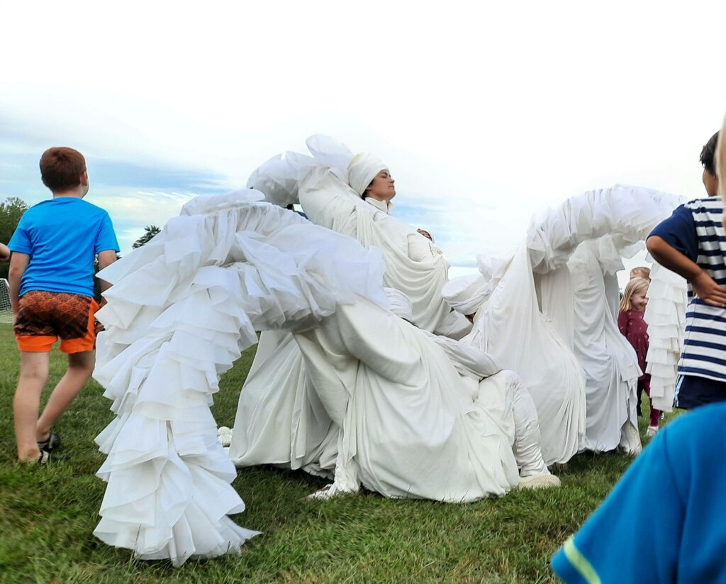 Picture of a performer dressed in flowing white looking proud as community members explore...